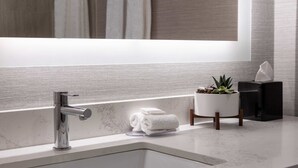 A modern bathroom with a large mirror, a chrome faucet, a marble sink, a small potted plant, and neatly folded towels on the counter.