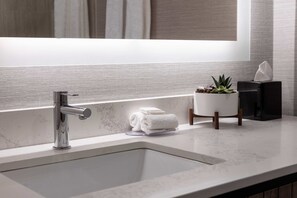 A modern bathroom with a large mirror, a chrome faucet, a marble sink, a small potted plant, and neatly folded towels on the counter.