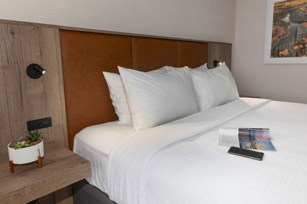 A neatly made bed with white bedding, a small bedside table with a plant, and a wall-mounted light.