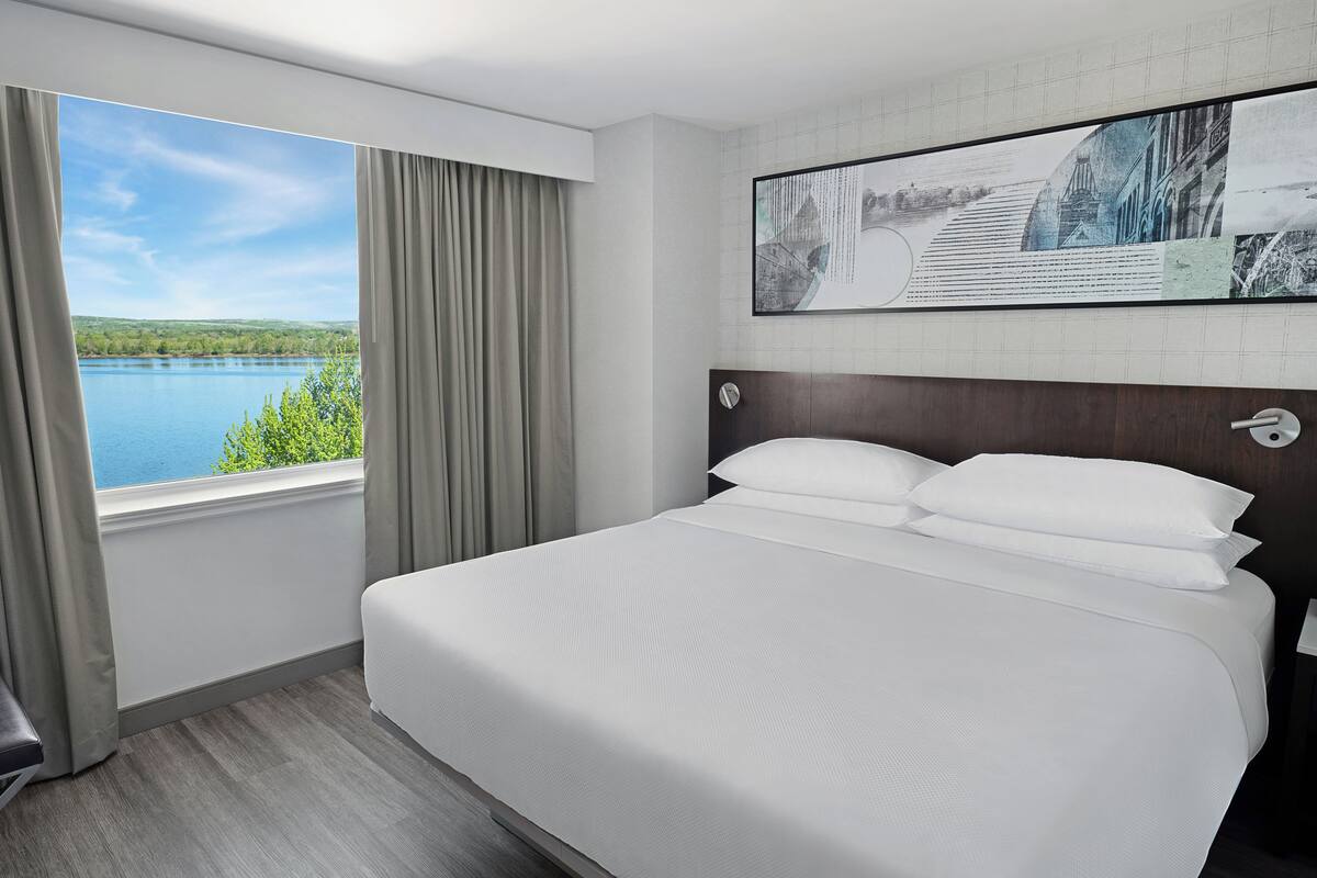Quarto de hotel com uma cama grande, vista para um lago e um quadro na parede.