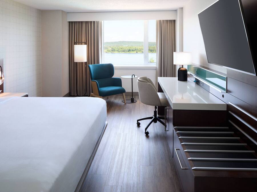 A hotel room with a bed, desk, chair, TV, and a view of a lake.