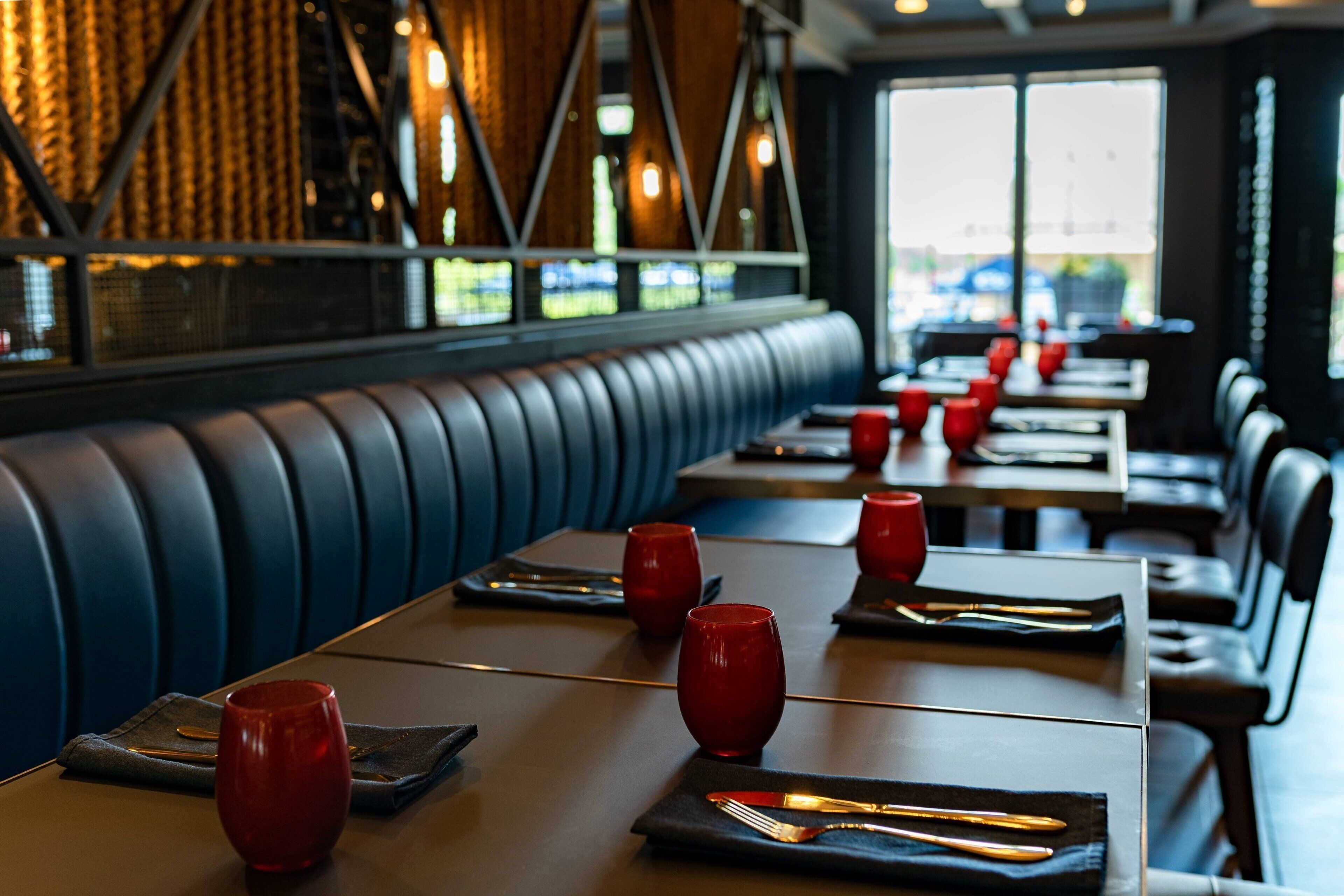 A restaurant interior with booths and tables, red napkins, and a view through the windows.
