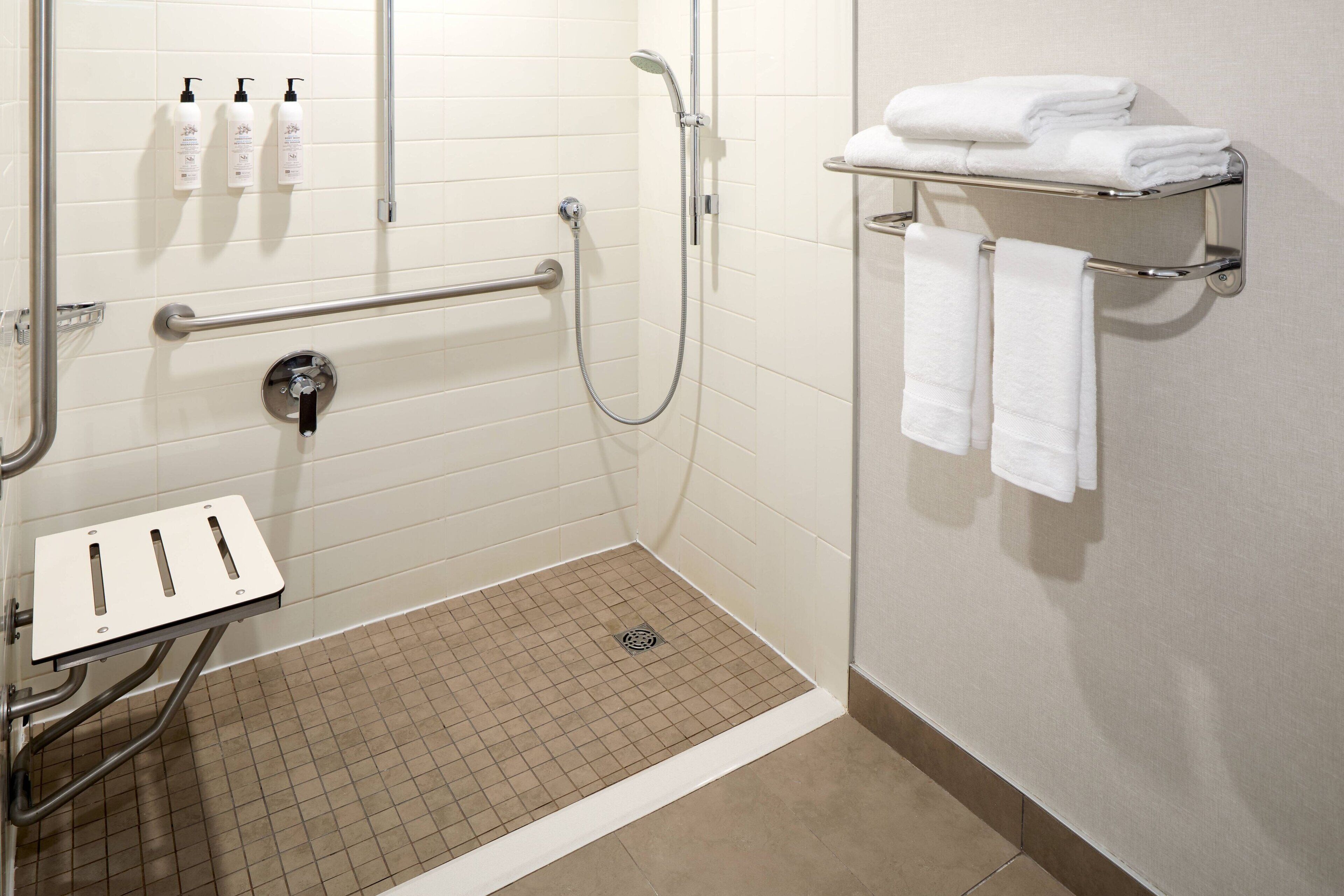 Une salle de bain équipée d’une douche, de barres d’appui, d’un porte-serviettes et d’un sèche-mains.