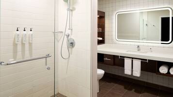 A modern bathroom with a glass-enclosed shower, white tiled walls, a large mirror with LED lighting, and a white sink with a towel rack.