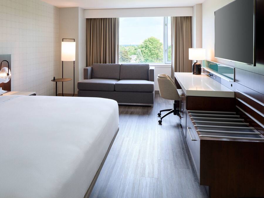 Habitación de hotel con una cama grande, un sofá, un escritorio con una silla, un televisor de pantalla plana y vistas al exterior.