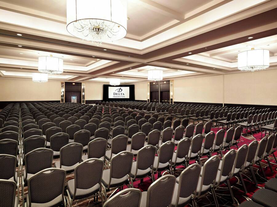 Une grande salle de conférence avec des rangées de chaises, une scène dotée d’un écran et des lustres.
