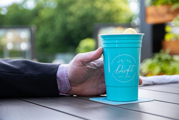 A hand holding a turquoise cup with a lemon slice on a wooden table.