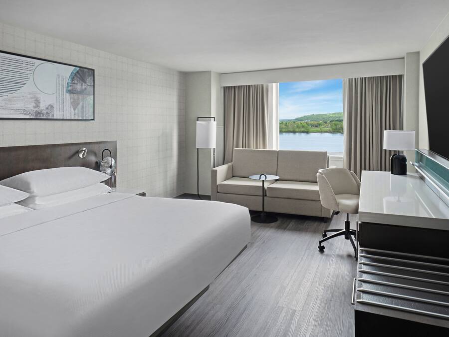 Quarto de hotel com uma cama grande, um sofá, uma escrivaninha e vista para um lago.