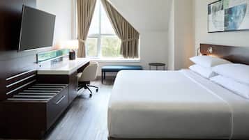 A hotel room with a bed, a desk, a chair, a TV, and a window with curtains.