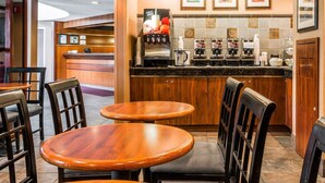 A hotel lobby with wooden furniture, a reception desk, and a coffee bar with multiple coffee machines. - Quality Inn Auburn Hills - Detroit North (Auburn Hills)