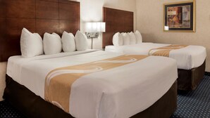 A hotel room with two beds, a large wooden headboard, a wall-mounted lamp, and a framed picture. - Quality Inn Auburn Hills - Detroit North (Auburn Hills)