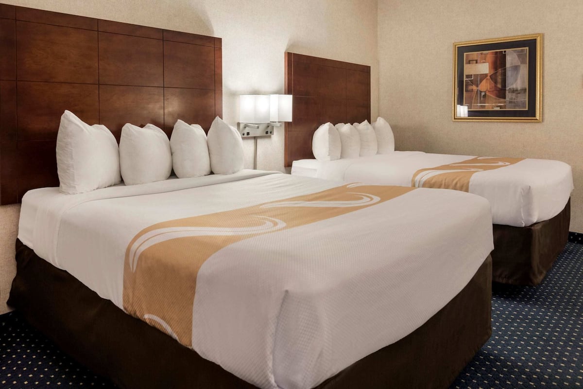 A hotel room with two beds, a headboard, a lamp, and a framed picture on the wall.