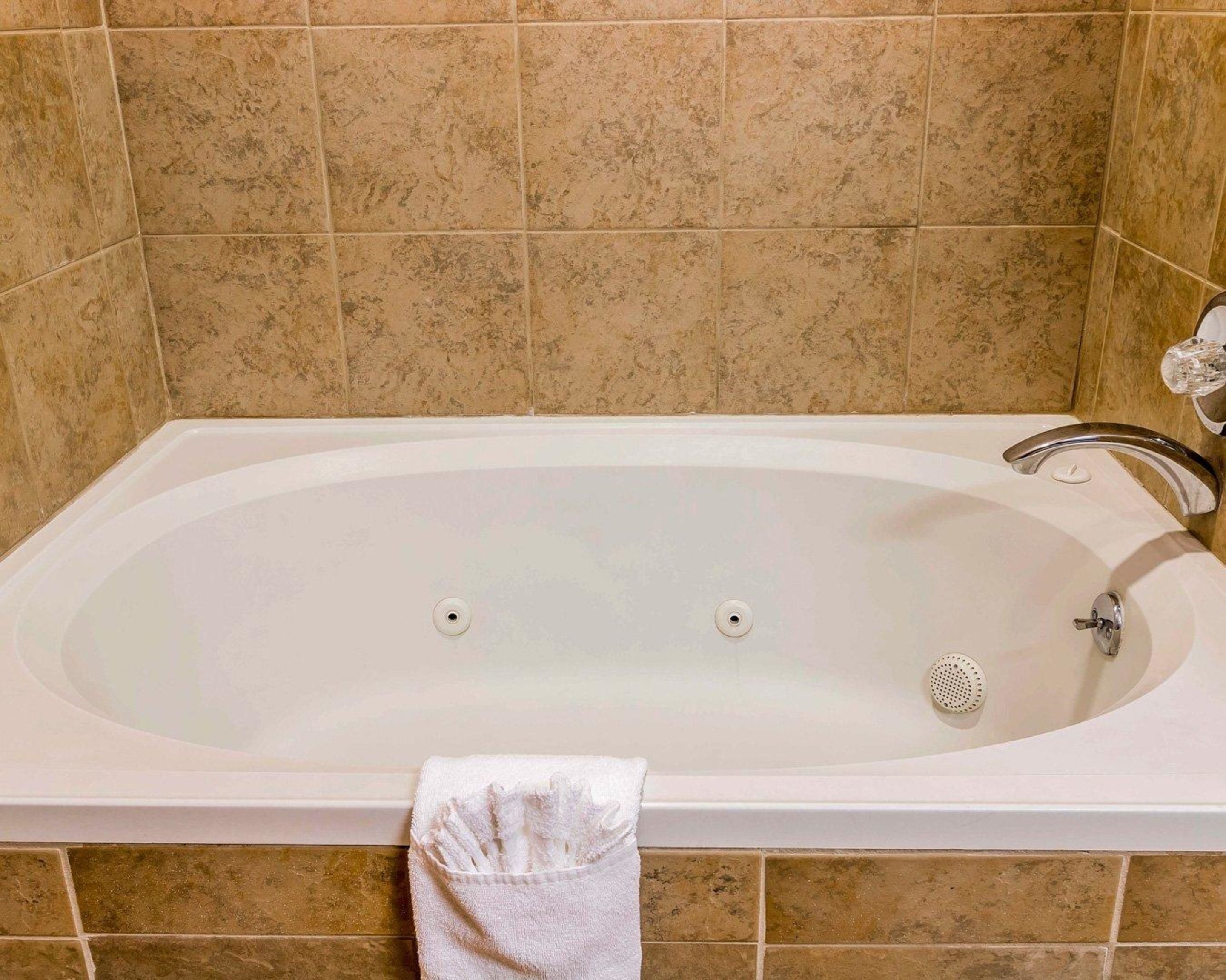 A rectangular bathtub with a single faucet and two drain holes, set against beige tiled walls.