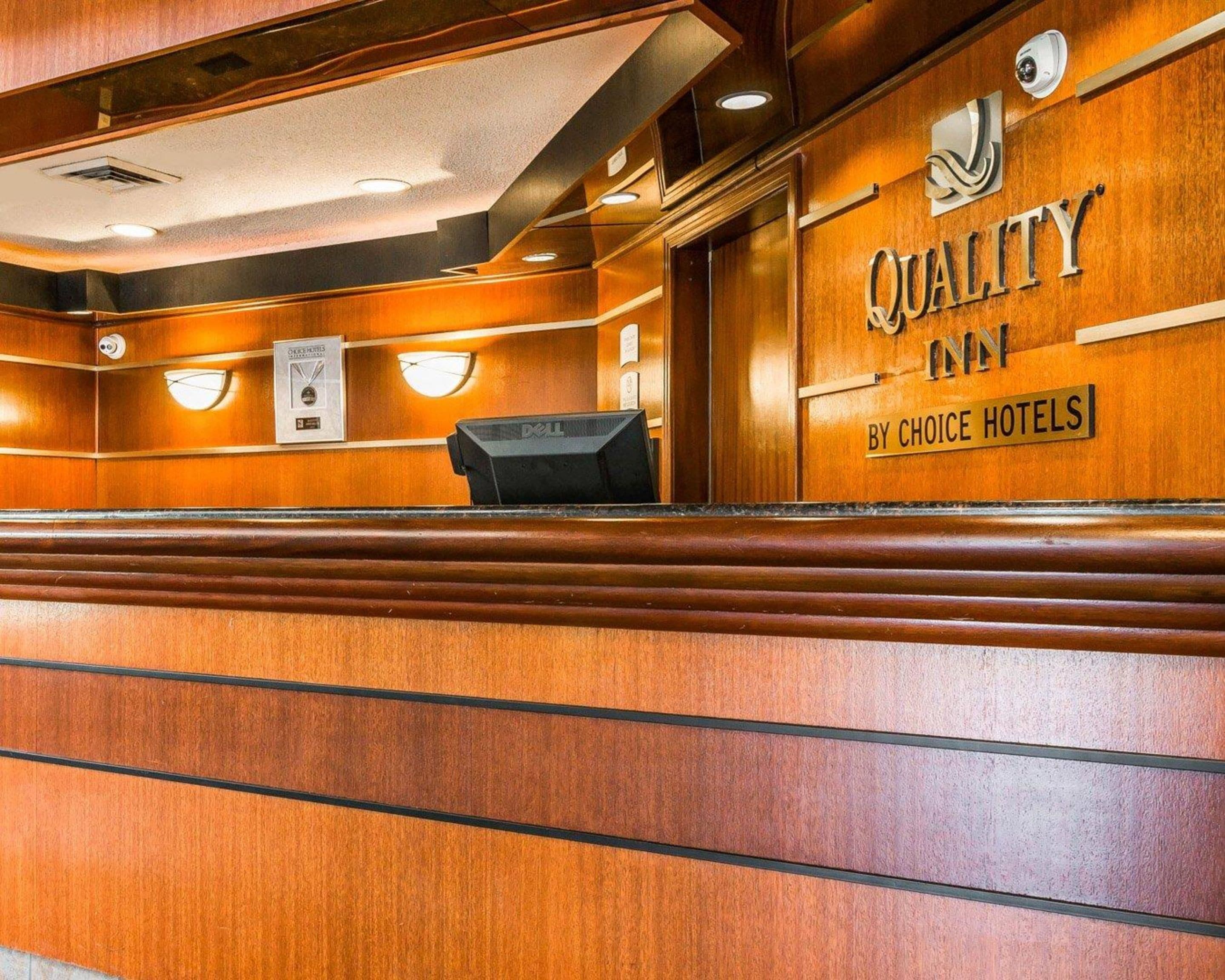 A reception area with a wooden finish, a sign reading "Quality Inn by Choice Hotels," and a desk with a computer.