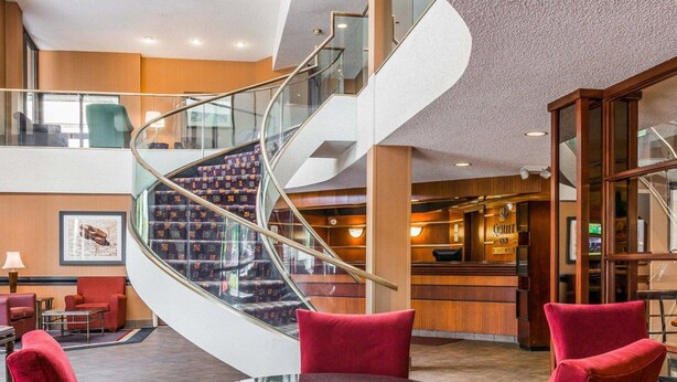 A hotel lobby with a spiral staircase, red upholstered chairs, a reception desk, and a glass coffee table. - Quality Inn Auburn Hills - Detroit North (Auburn Hills)