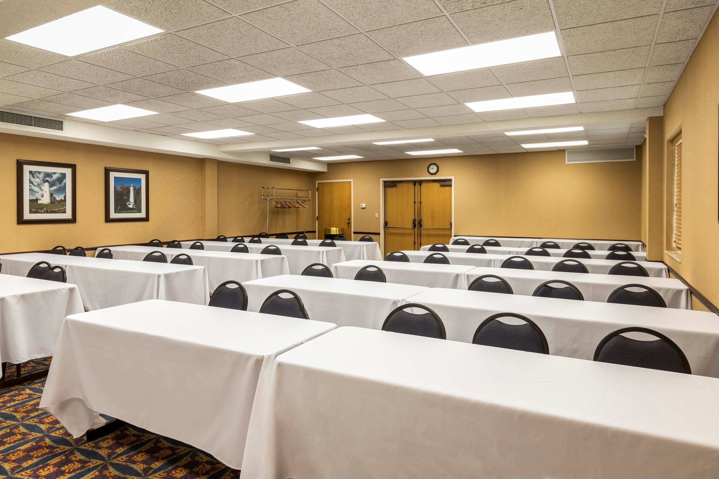 Une salle de conférence équipée de plusieurs tables et chaises, avec une horloge au mur et des photos encadrées de phares.