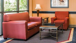 A hotel room with a red leather sofa, a matching armchair, a small table, and a lamp. A framed map is on the wall. - Quality Inn Auburn Hills - Detroit North (Auburn Hills)