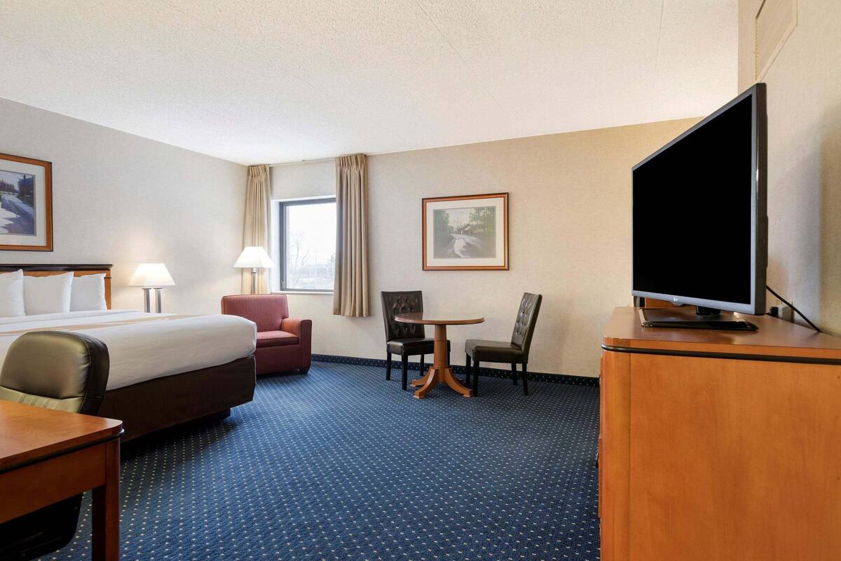 A hotel room with a bed, a desk, a television, and two chairs.
