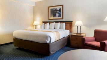 A hotel room with a large bed, two bedside tables with lamps, a chair, and a framed picture on the wall.