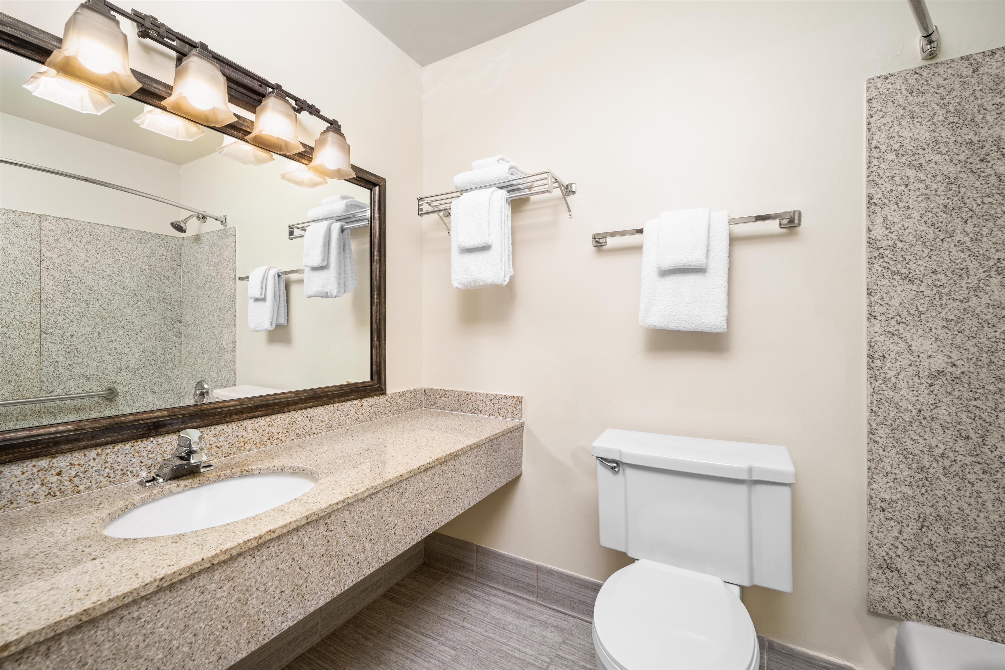 A bathroom with a granite countertop sink, a white toilet, and a towel rack with white towels.