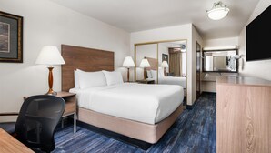 Habitación de hotel con una cama grande, dos mesitas de noche con lámparas, un escritorio con una silla, un espejo y un televisor de pantalla plana.