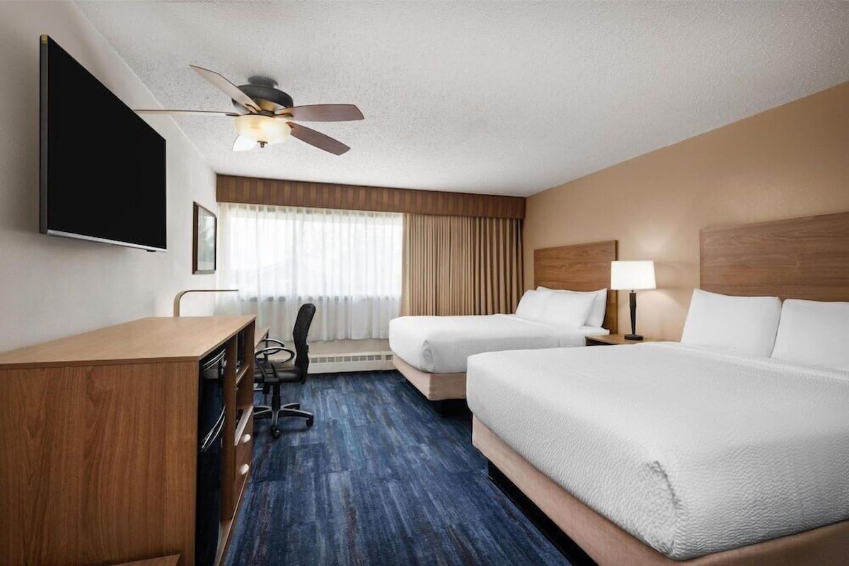 Habitación de hotel con cama, escritorio, silla, televisor, ventilador de techo y ventana con cortinas.