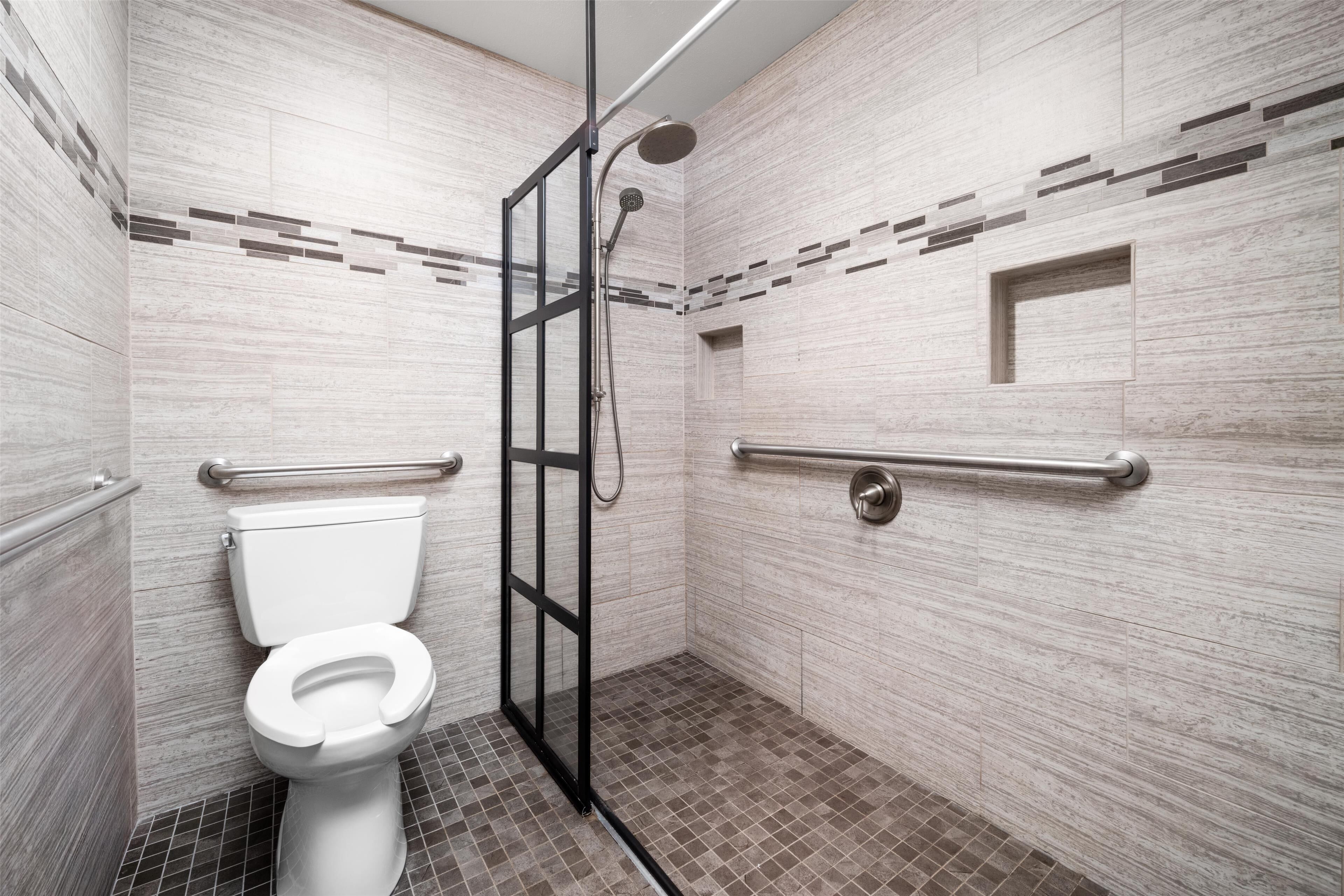 A modern bathroom with a shower, toilet, and grab bars.