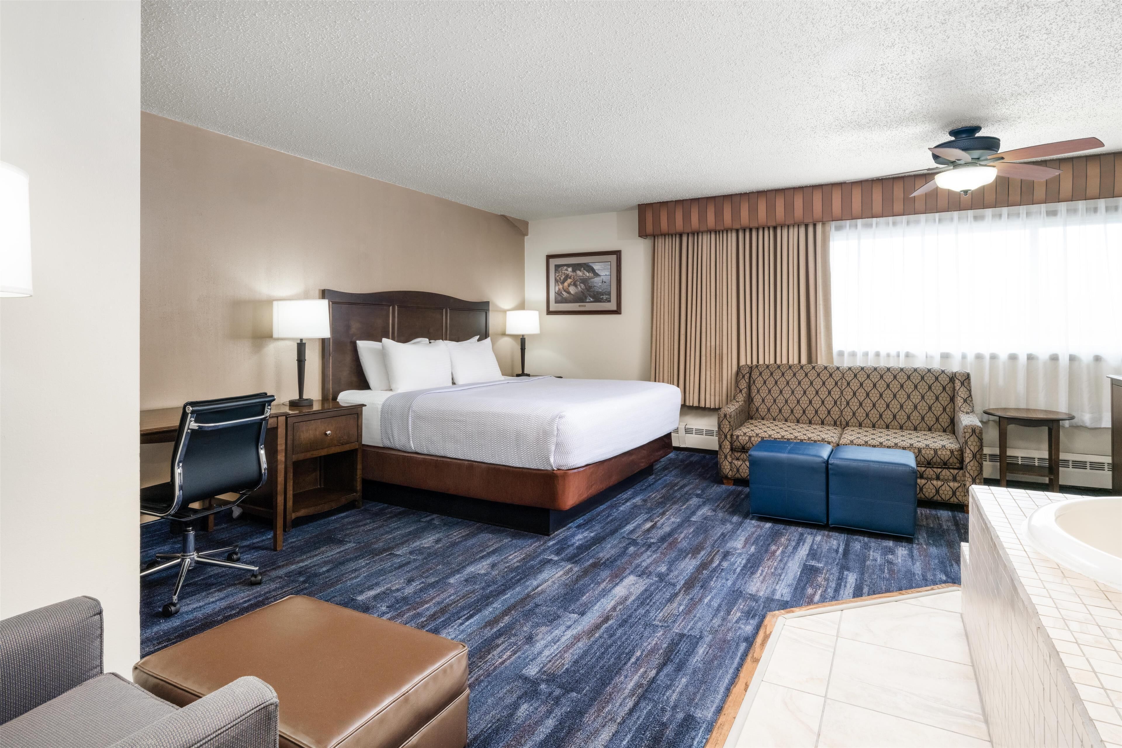 Ein Hotelzimmer mit Bett, Schreibtisch, Stuhl, Hocker und einem Badezimmer mit Badewanne.