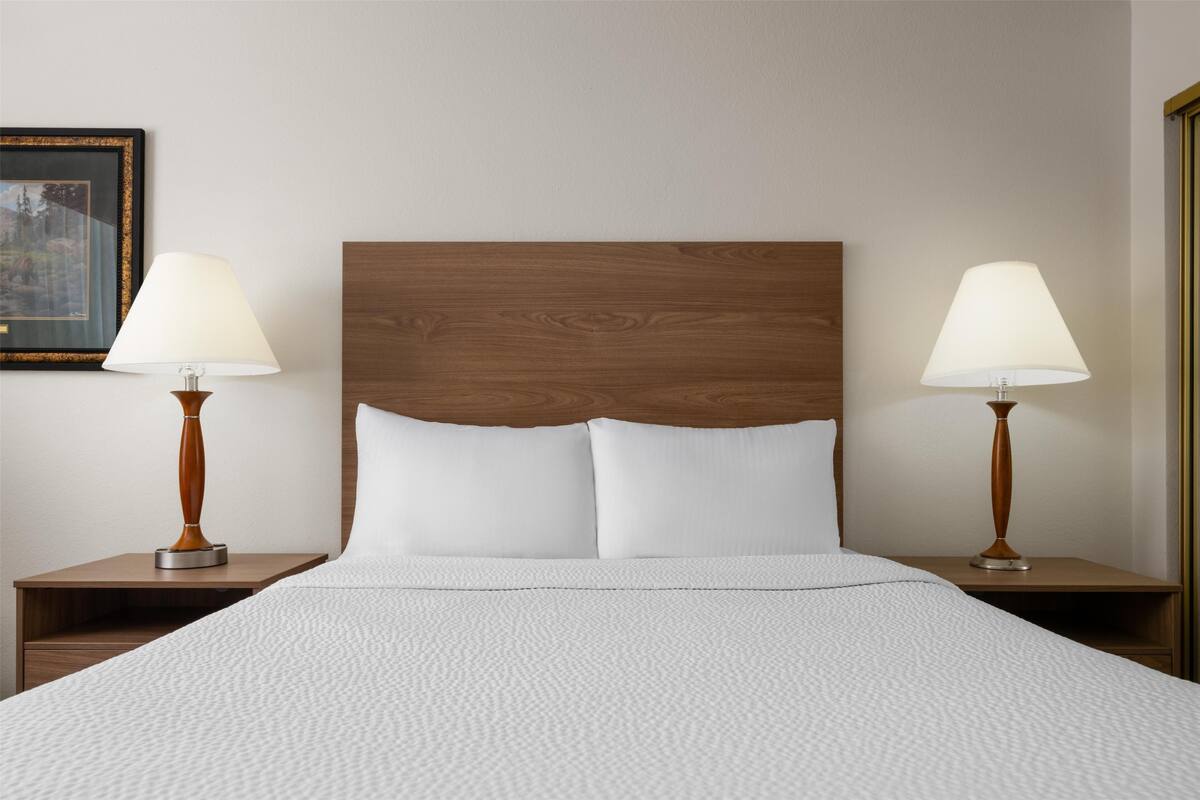 Una cama bien hecha con cabecera de madera, flanqueada por dos mesitas de noche con lámparas.
