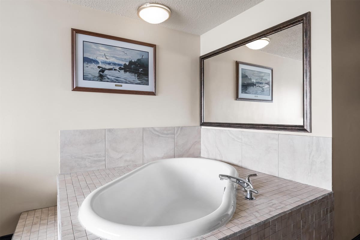 Un baño con una bañera grande, un espejo y dos cuadros enmarcados en la pared.