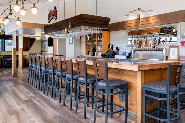 Una zona de bar con taburetes de madera, una barra con caja registradora y un grifo de cerveza.