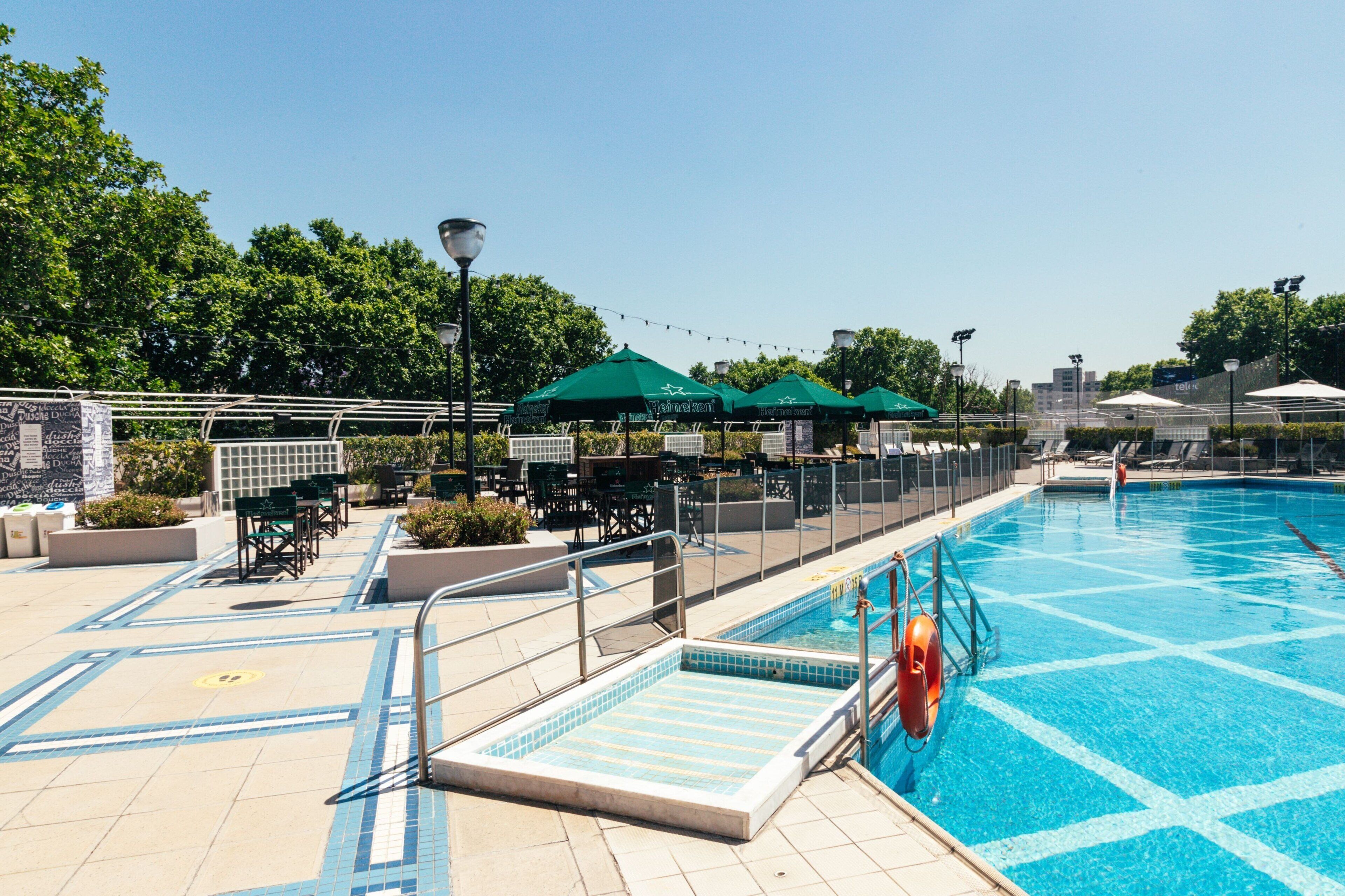 A rooftop pool area with a diving board, lounge chairs, and umbrellas.