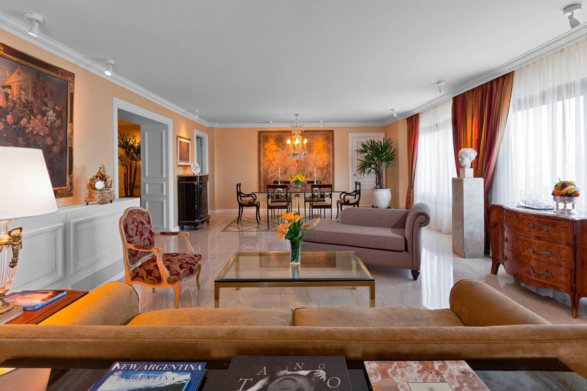 Ein geräumiges Wohnzimmer mit Sofa, Sesseln, einem Couchtisch und einem Essbereich mit Stühlen und einer Kristallleuchter.