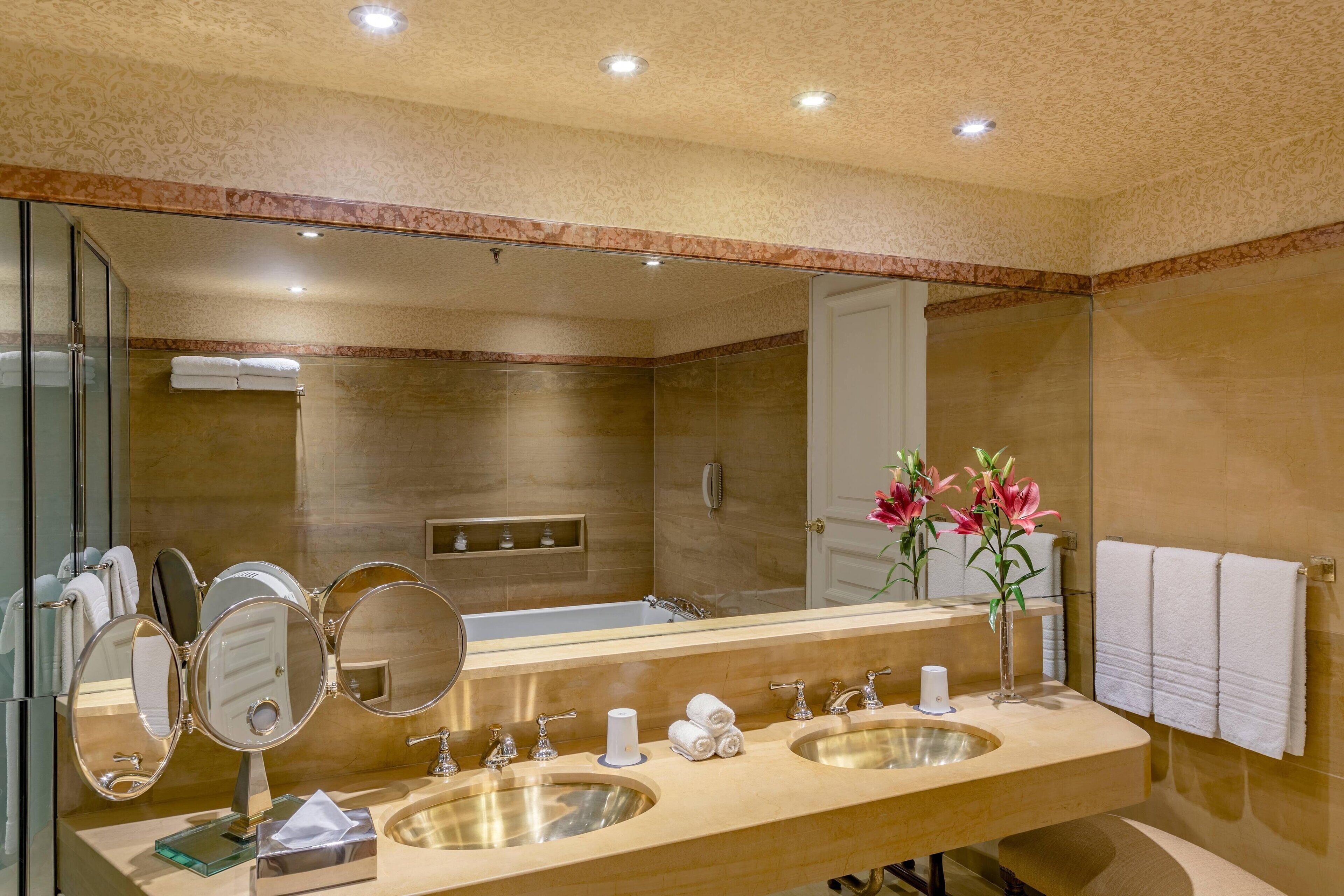 A modern bathroom with a double sink, three mirrors, a large mirror, and a shower area.