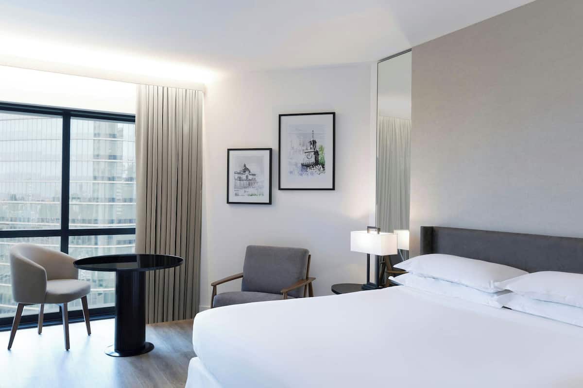 Ein Hotelzimmer mit einem großen Bett, zwei Sesseln, einem kleinen Tisch, einer Lampe und zwei gerahmten Bildern an der Wand.