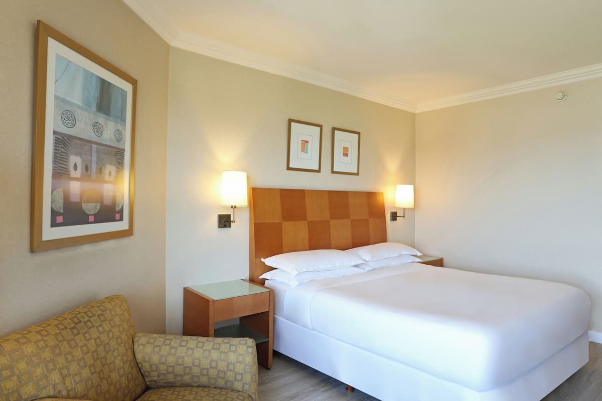 Ein Hotelzimmer mit einem großen Bett, zwei Nachttischlampen, einem Nachttisch, einem gemusterten Sessel und zwei gerahmten Bildern an der Wand.