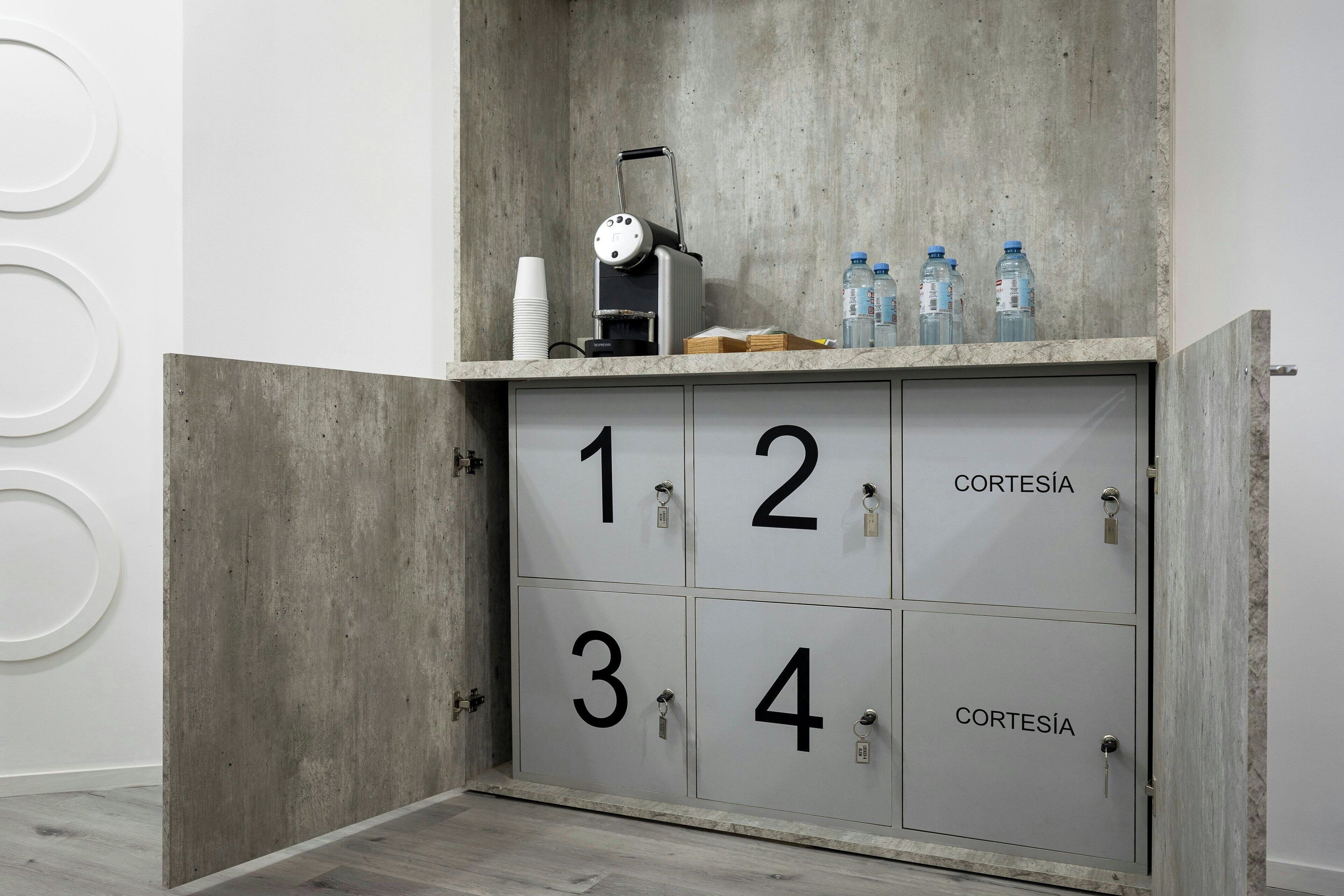 Un armadietto contenitore con scomparti numerati, con l'etichetta 'CORTESÍA' e un elettrodomestico sopra.