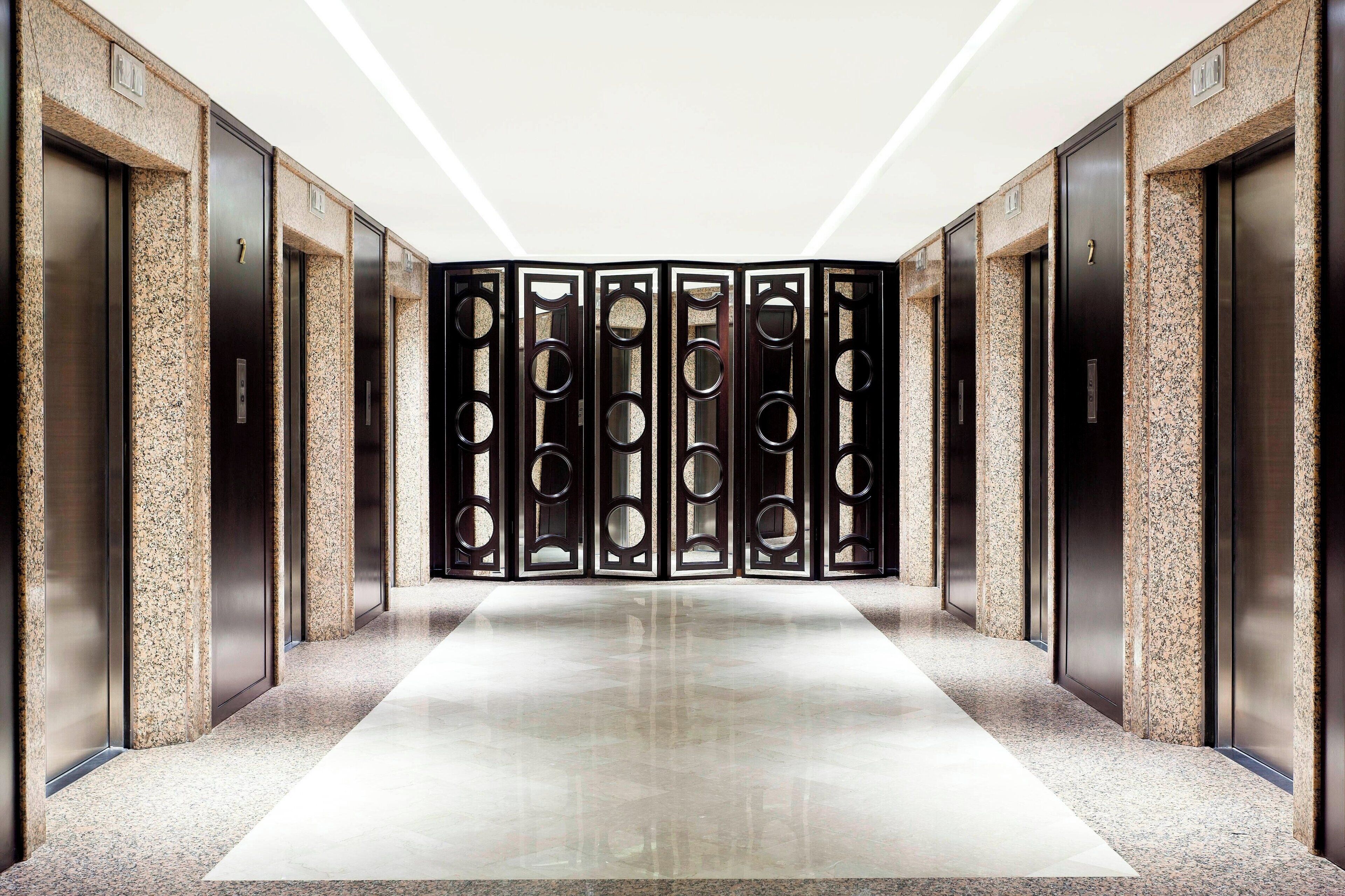 A modern elevator lobby with a polished floor and a central divider with circular cutouts.