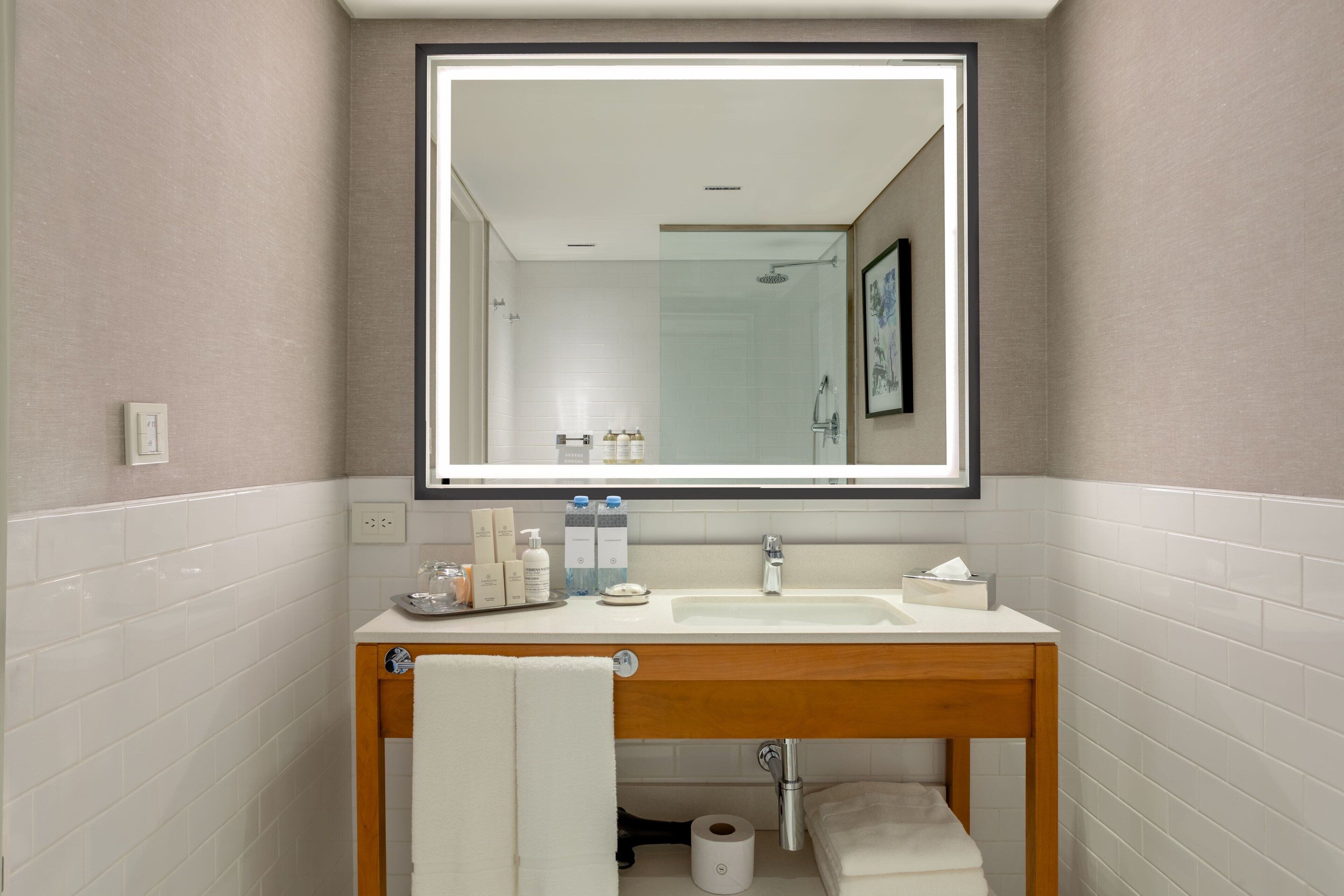 A modern bathroom with a large mirror, white tiles, a wooden vanity, and a toilet.