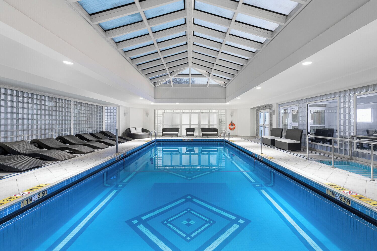 An indoor swimming pool with a skylight ceiling, lounge chairs, and a lifebuoy.
