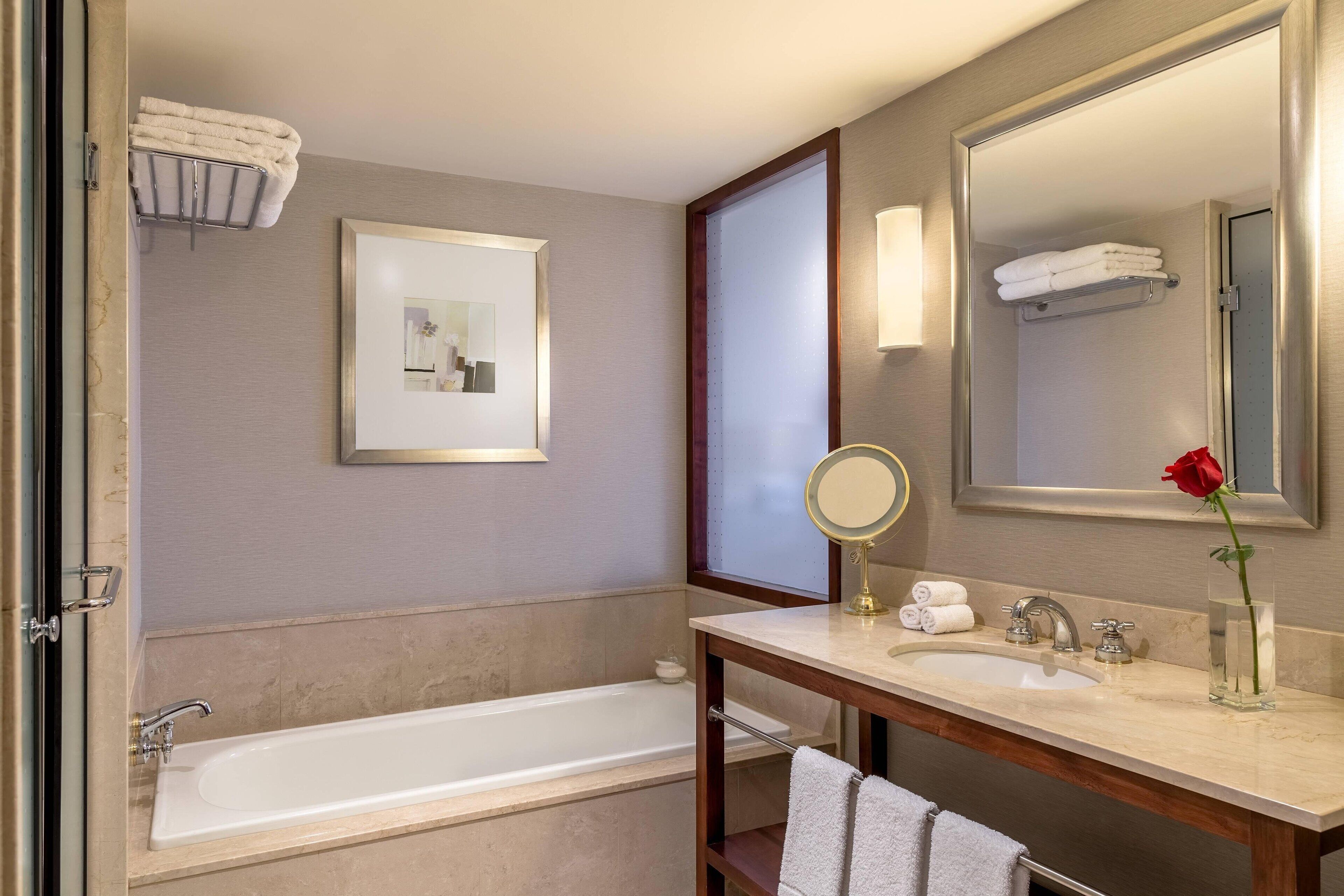 A modern bathroom with a bathtub, a sink, a mirror, and a framed picture on the wall.