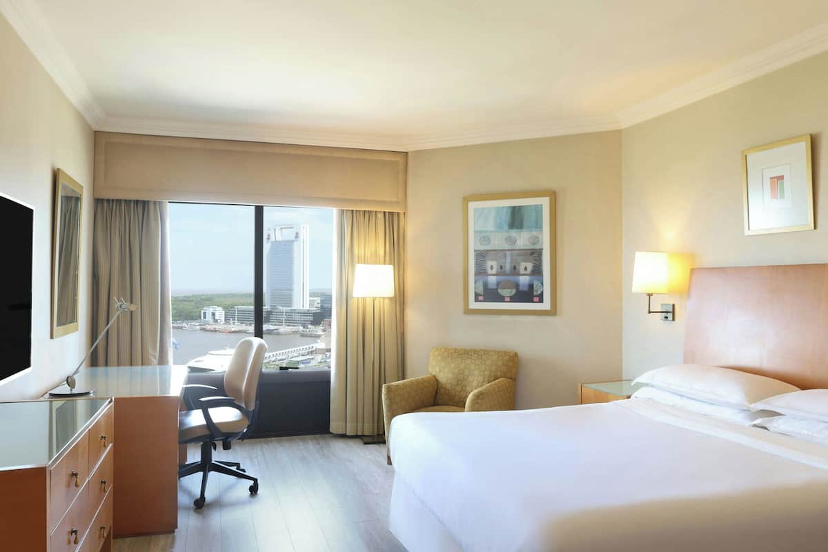 Ein Hotelzimmer mit Bett, Schreibtisch, Stuhl und einem großen Fenster mit Blick auf die Stadt.