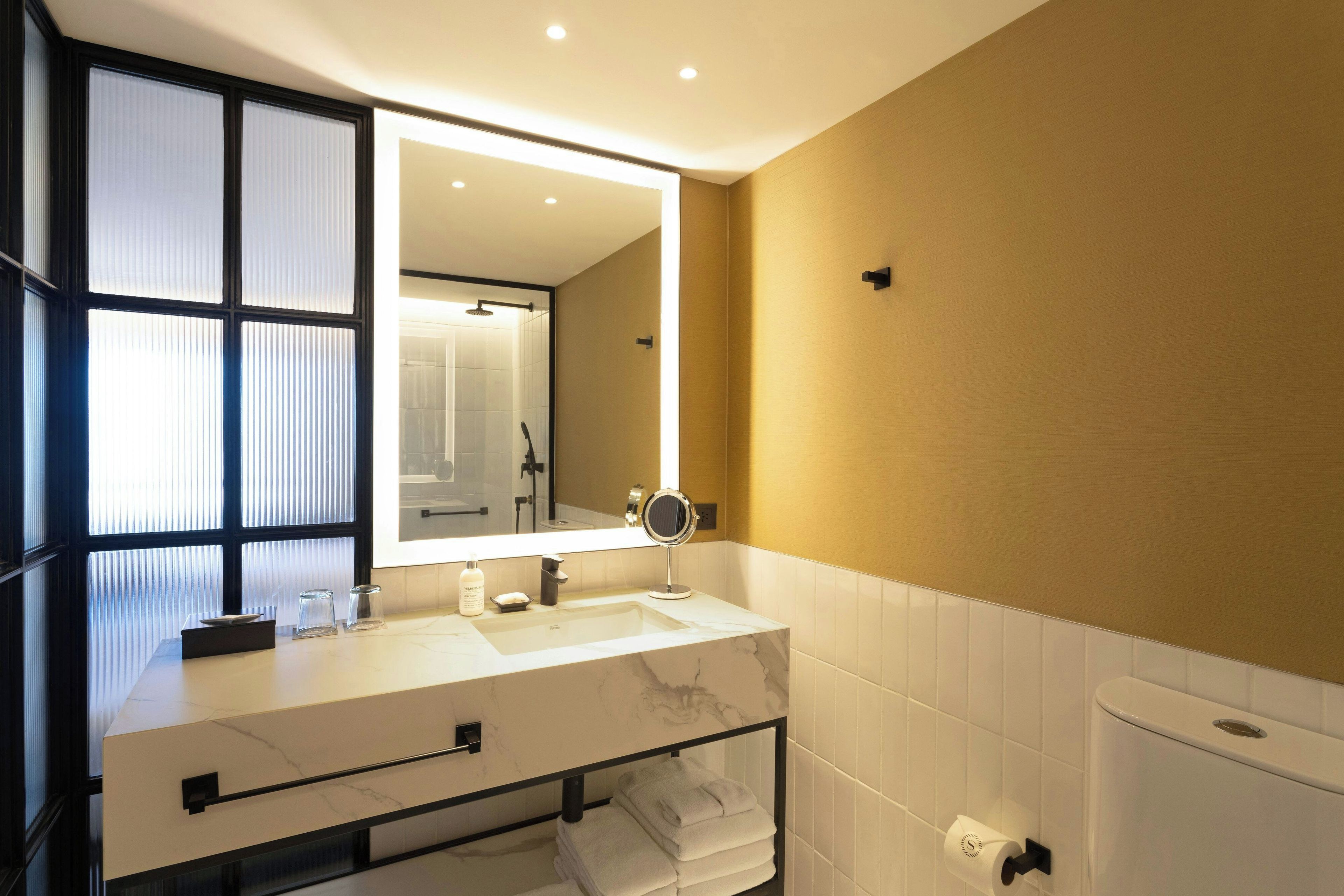 Un baño moderno con un lavabo de mármol blanco, un espejo grande y un perchero para toallas.