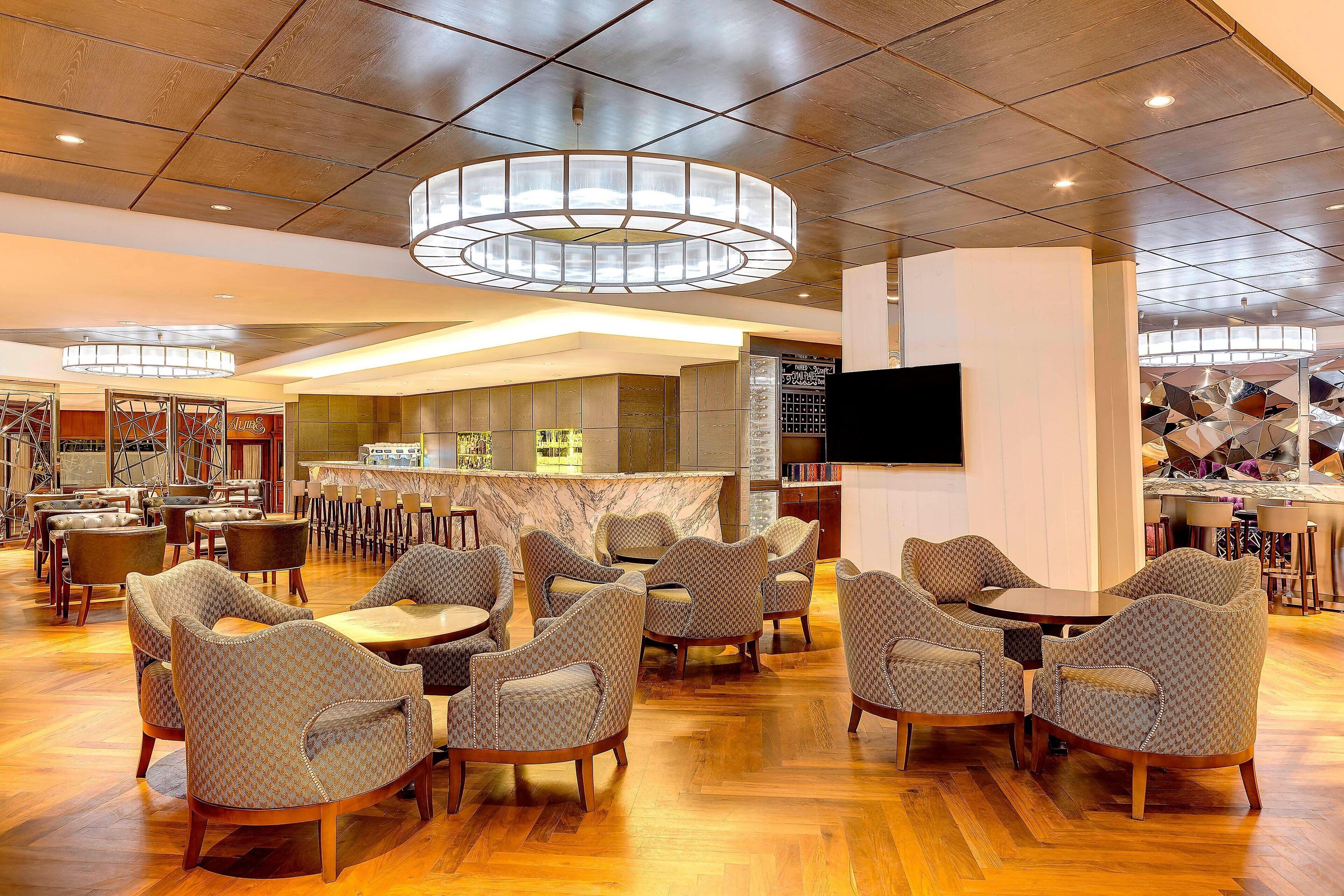 Een ruime lobby met een bar in het midden, verschillende zithoeken en een moderne kroonluchter.