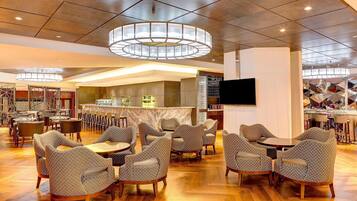 Een ruime lobby met een bar in het midden, verschillende zithoeken en een moderne kroonluchter.