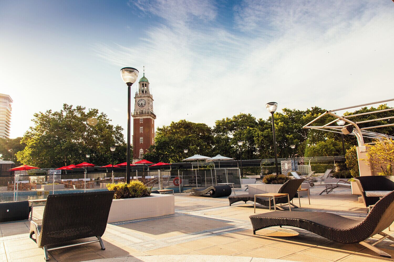 Een terras met lounge fauteuils en parasols, met een klokkentoren op de achtergrond en een heldere lucht.