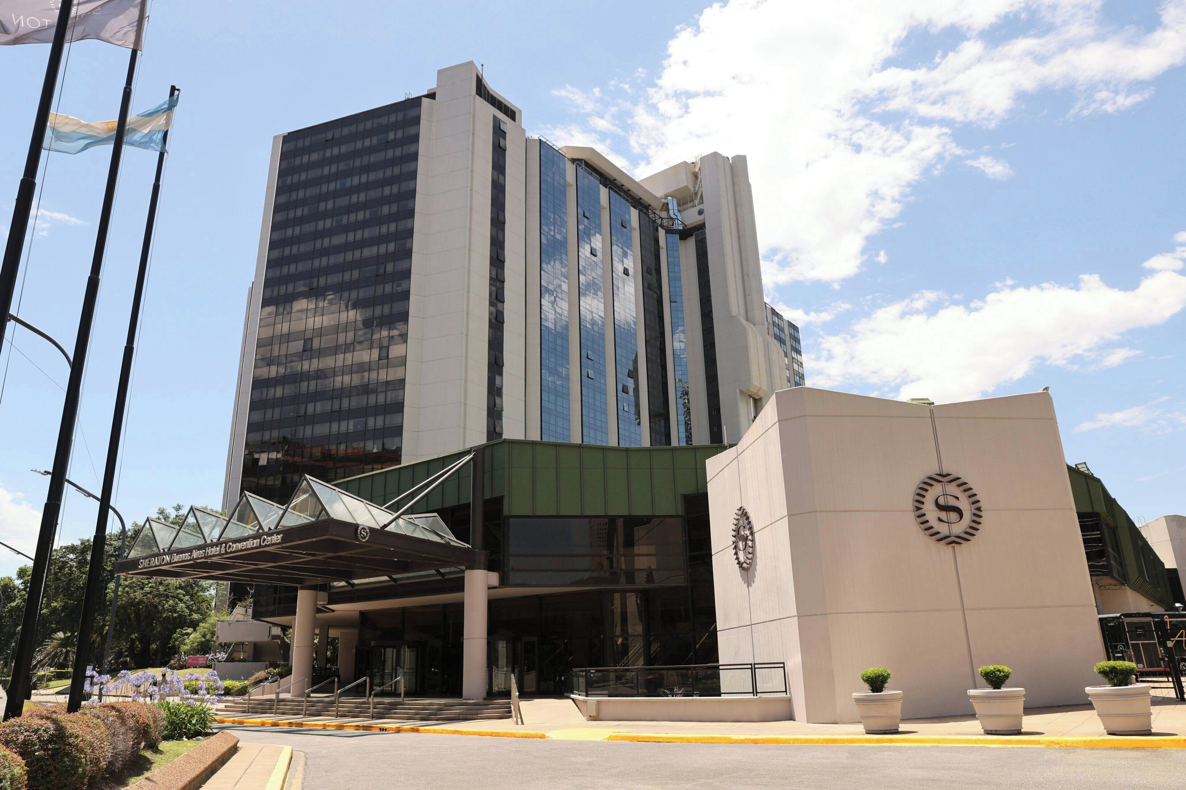 A modern building with a glass facade, a prominent entrance with a covered area, and a clock on the side.