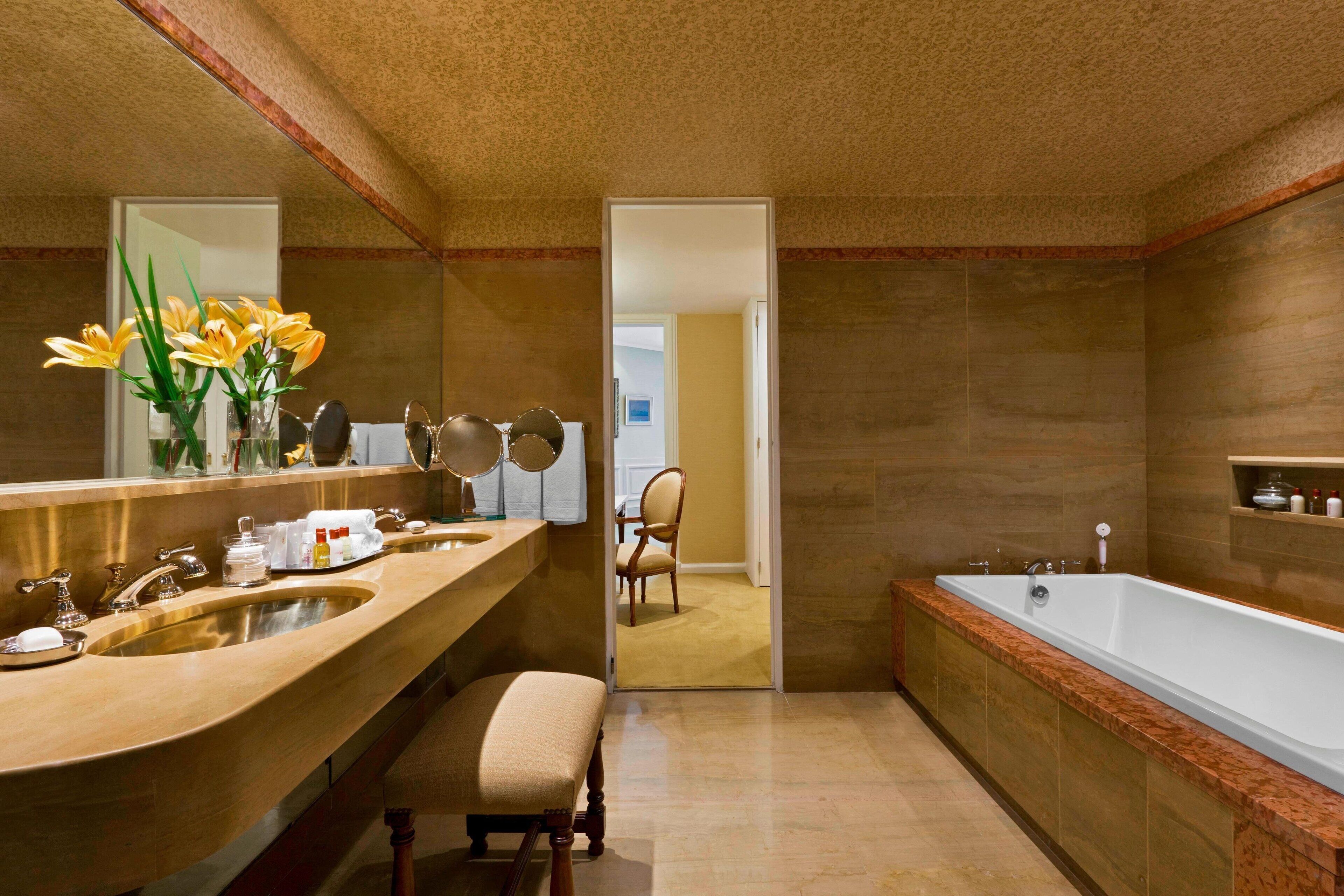 A bathroom with a double sink vanity, a large mirror, a bathtub, and a chair.