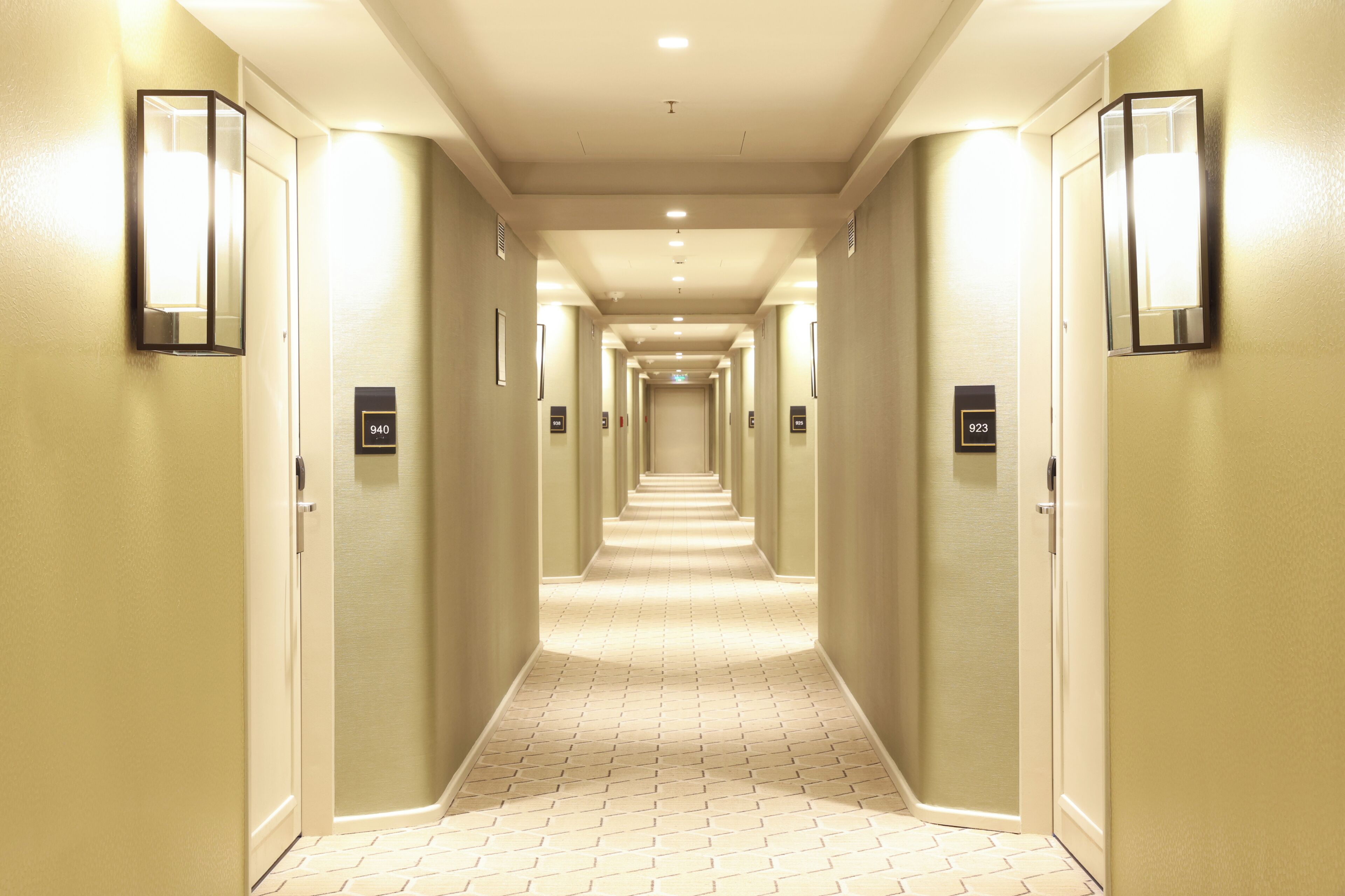 A hotel hallway with a tiled floor, light-colored walls, and numbered doors.