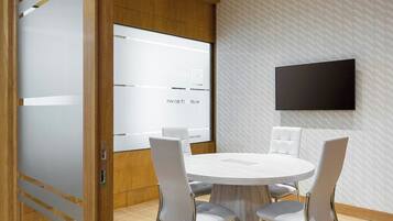 Una sala de reuniones moderna con una mesa redonda, sillas blancas, vigas de madera en el techo y un televisor montado.